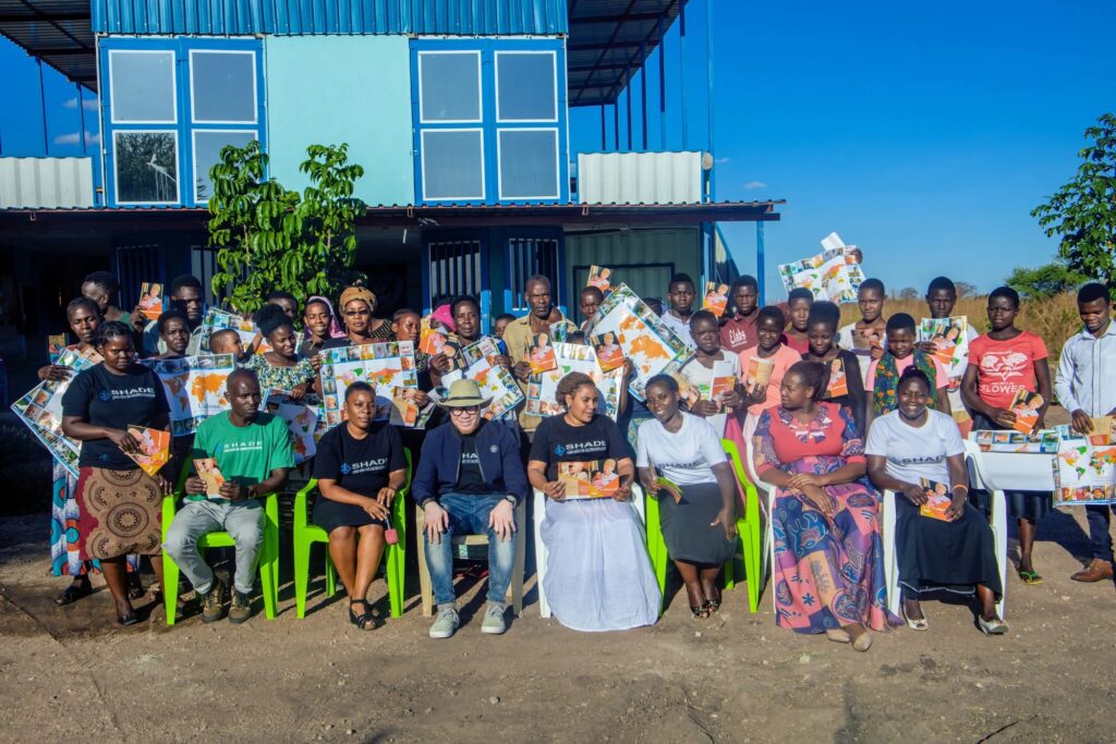 Group of people holding posters and booklets, standing and sitting in front of a blue building.
